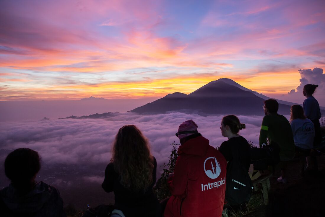 Leader with travellers enjoying the view of a purple sunrise during a Mount Batur hike in Bali, Indonesia