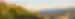 A church sits on a hill filled with trees in Romania and the hill descends into the valley village.