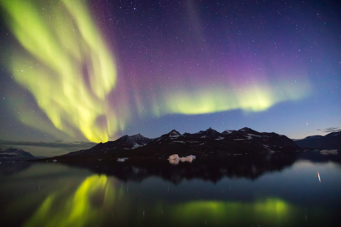 Yellow green and magenta waves of iridescent northern lights undulate over the Greenland landscape at twilight