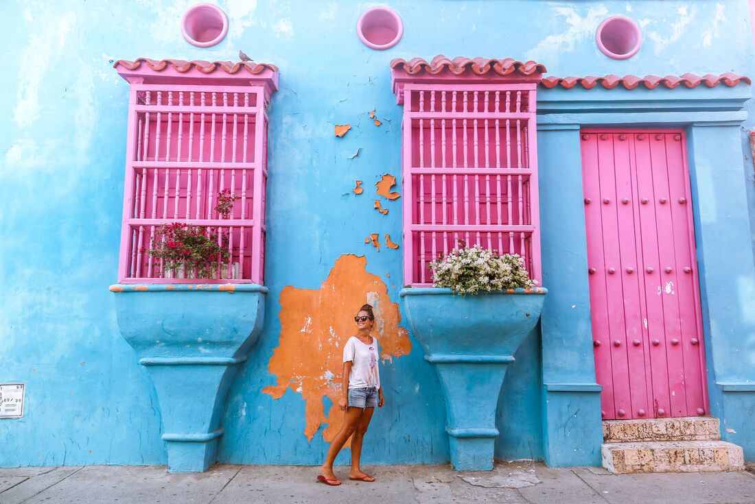 Traveller smiling in front of bright blue and pink building in Cartagena, Colombia